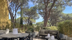 Een terras buiten met ronde tafels en stoelen, een bank en een kleine ronde tafel met een kaars.
