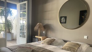 Een slaapkamer met een bed, kussens, een nachtkastje, een lamp, een spiegel en een potplant.
