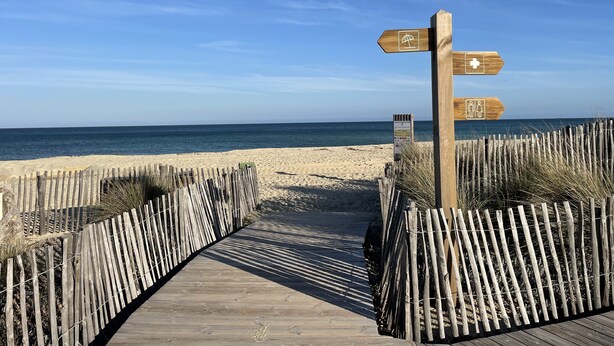 Een houten looppad dat naar een strand leidt, met richtingaanwijzingen.