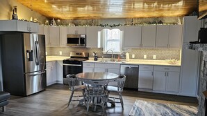 Een moderne keuken met een centraal eiland, roestvrijstalen apparatuur en een eethoek met een ronde tafel en stoelen.