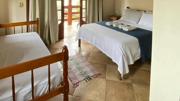 A room with two beds, a wooden ceiling, and a view through a door. - Estalagem São Gonçalo  (Paraty)