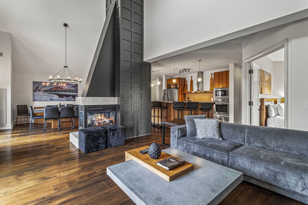 Un salón moderno con chimenea, un sofá gris y un comedor con vistas a la cocina.