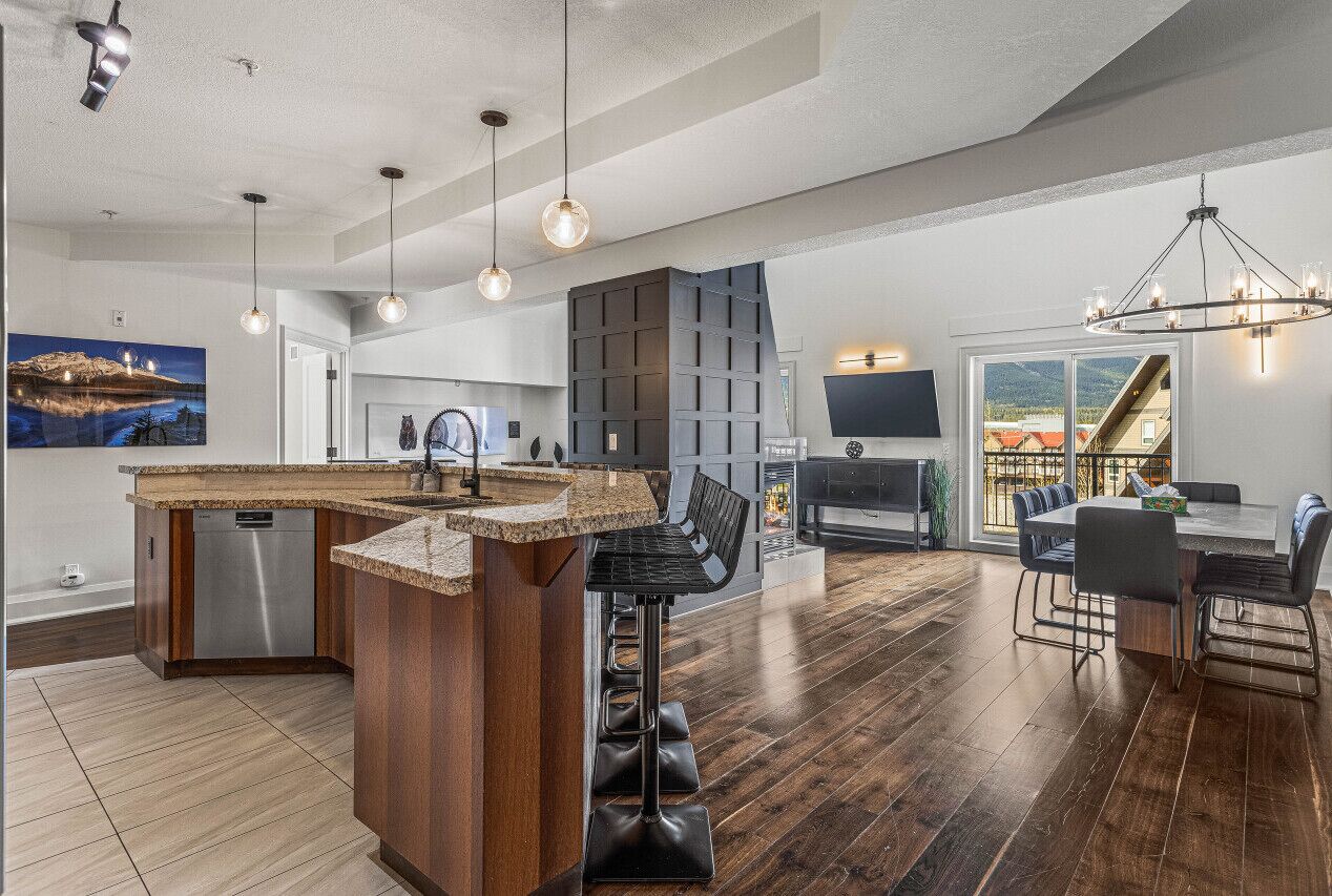 Una cocina moderna con una isla central, taburetes de bar y un comedor con una mesa grande y sillas.