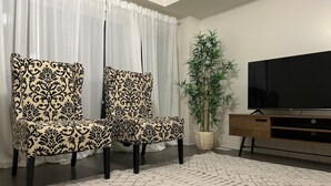 Een woonkamer met twee gestreepten fauteuils, een televisie, een houten kast en een potplant.