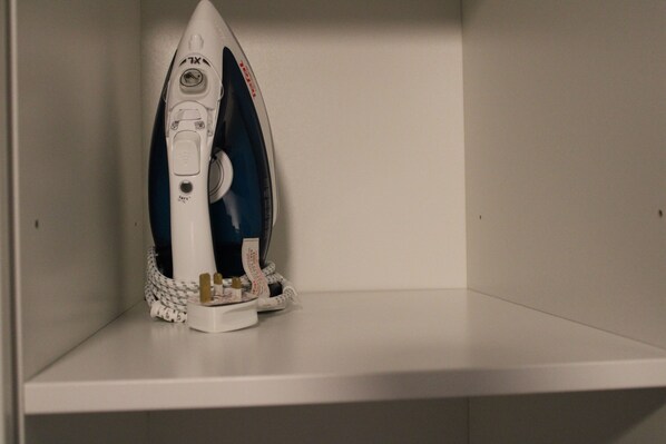 A white ironing board with an iron and a clothespin holder on a white shelf.
