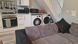 Eine moderne Küche mit Einbauofen, Mikrowelle und Waschmaschine. Es gibt eine Couch mit Kissen und eine Treppe, die in ein Obergeschoss führt.