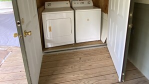 Una lavanderia con due lavatrici, uno scaffale di legno con una tettarella e una porta con maniglia in ottone.