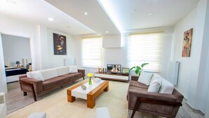 A spacious living room with a brown sofa, white sofa, and a coffee table. There is a TV and a plant in the room. - SEYİR ROYAL (Kocasinan)