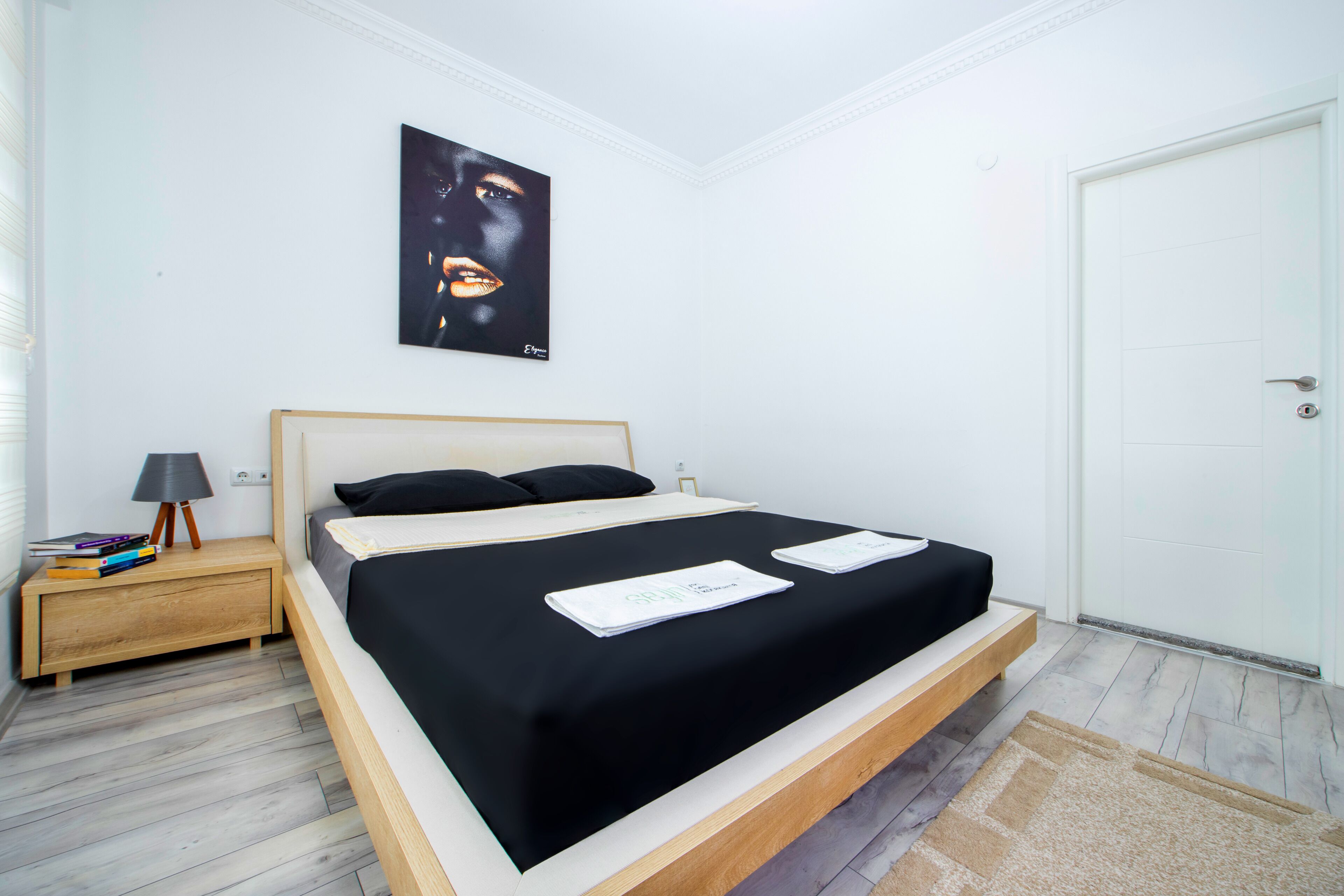 A bedroom with a bed, a nightstand, a lamp, a framed picture on the wall, and a door.