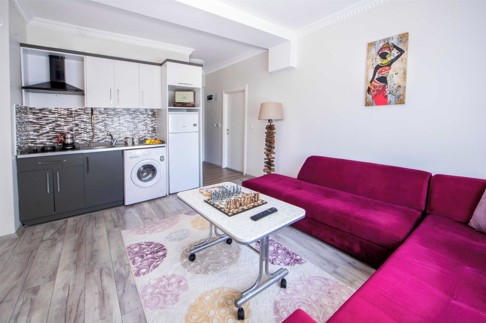 A compact living space with a kitchenette, a red sofa, and a small table with a chess set.