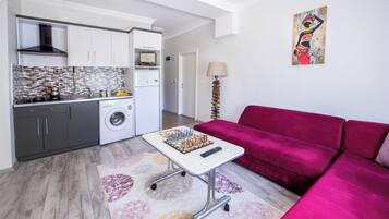 A compact living space with a kitchenette, a red sofa, and a small table with a chess set.