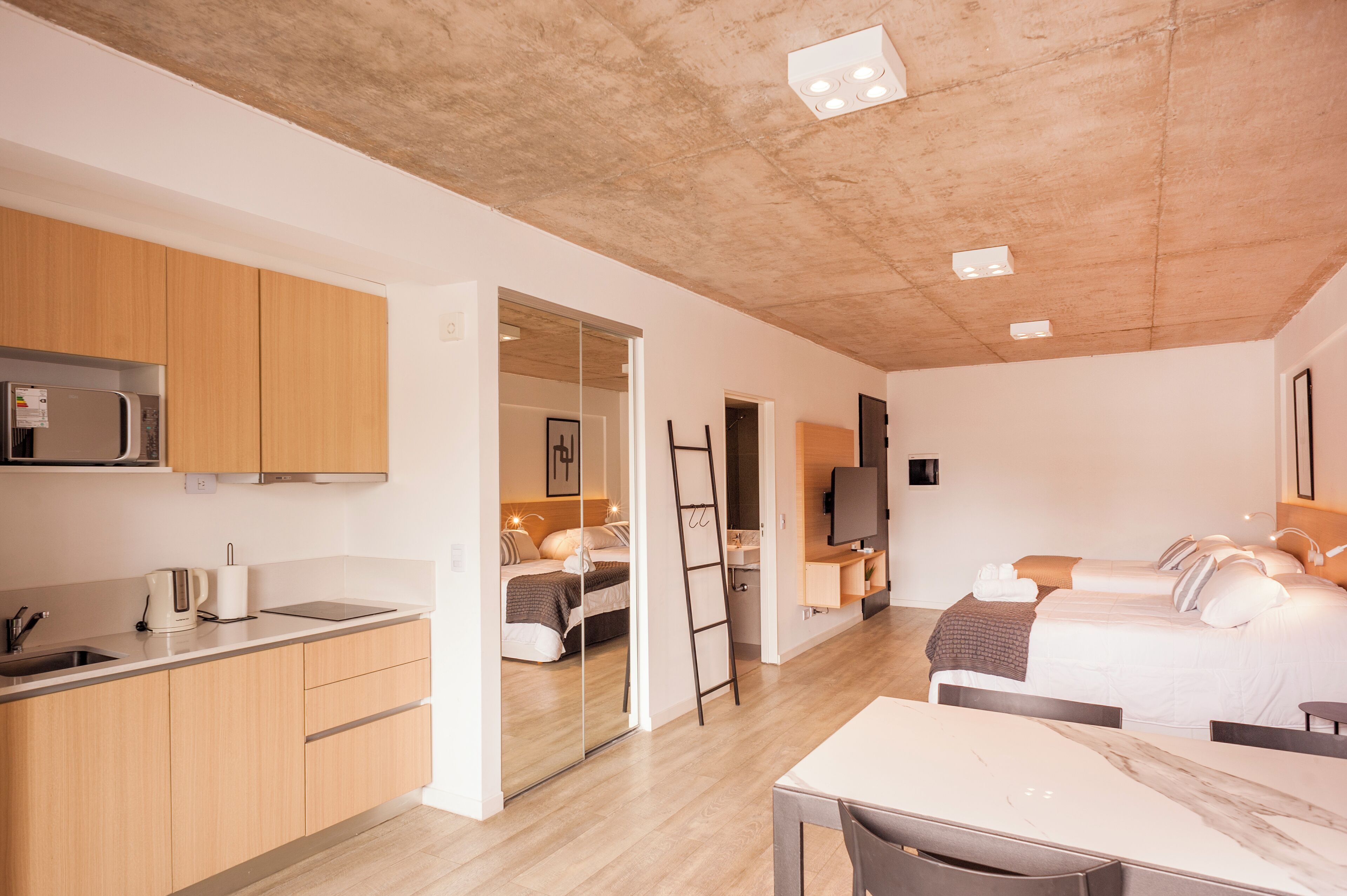 Une pièce moderne et bien éclairée, comprenant une cuisine, un coin repas et une chambre avec un grand lit et une télévision.