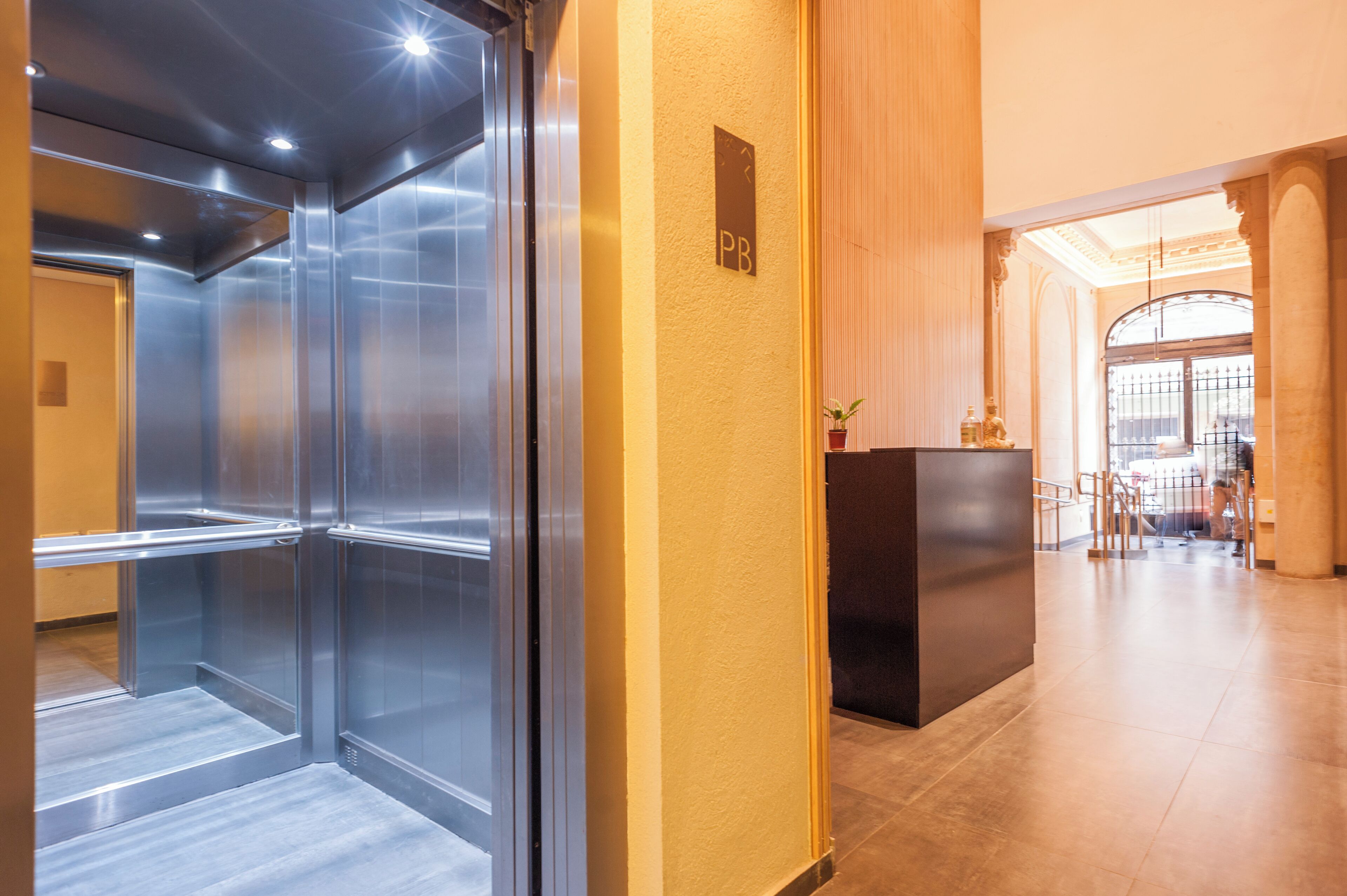 A modern elevator with glass doors, a reception desk, and a well-lit hallway leading to an entrance.