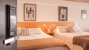 Habitació d'hotel amb dos llits, un rellotge digital penjat a la paret i obra d'art emmarcada.
