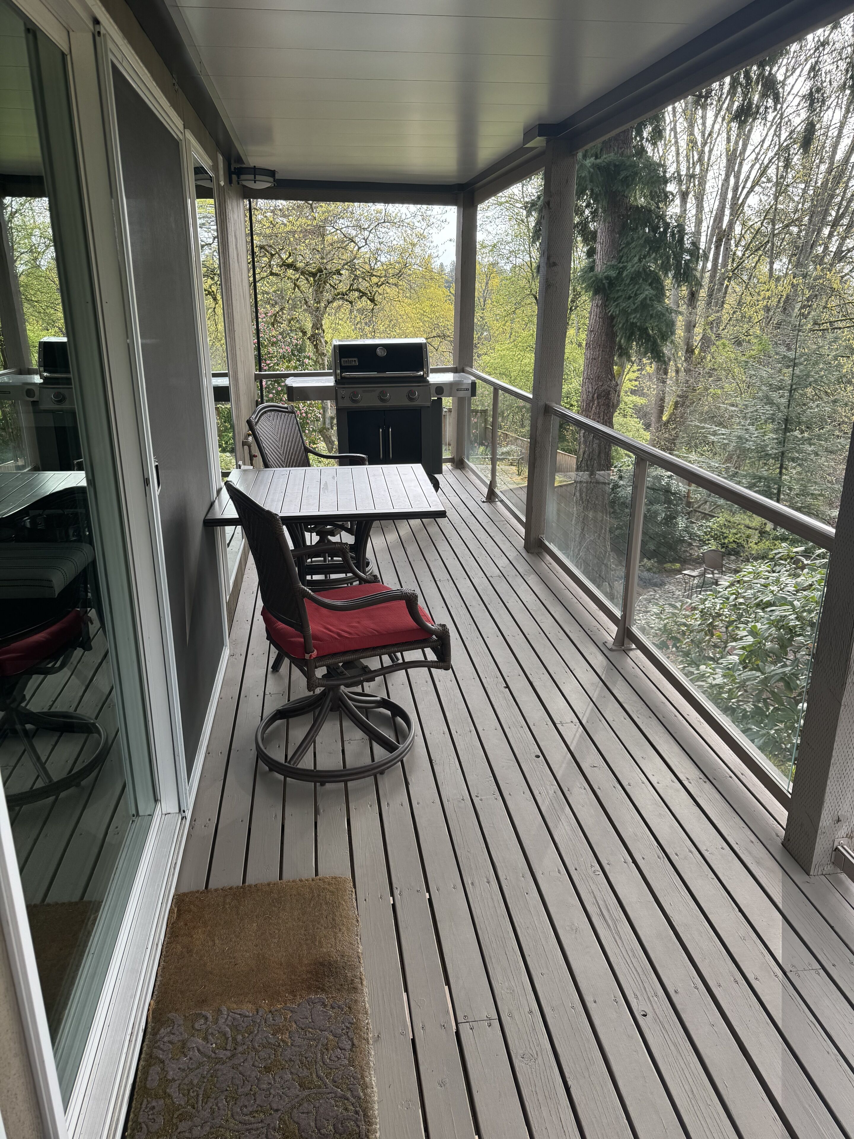 Un espace extérieur abrité, équipé d’une table et de chaises, d’un barbecue et offrant une vue sur les arbres.
