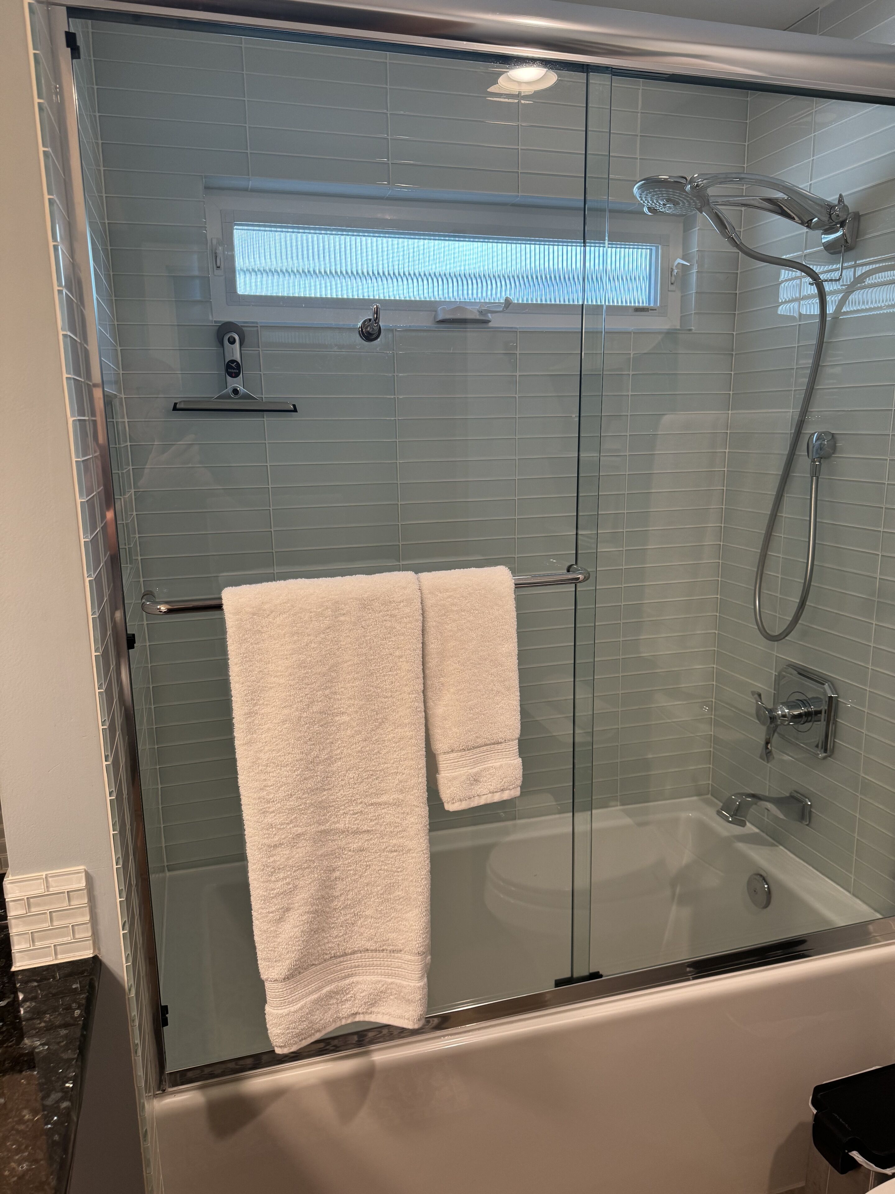 Une douche fermée par des parois en verre, équipée d’un pommeau de douche à main et d’un flexible de douche.