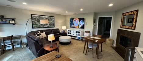A living room with a sofa, ottoman, coffee table, TV, fireplace, and a dining area with chairs and a table.