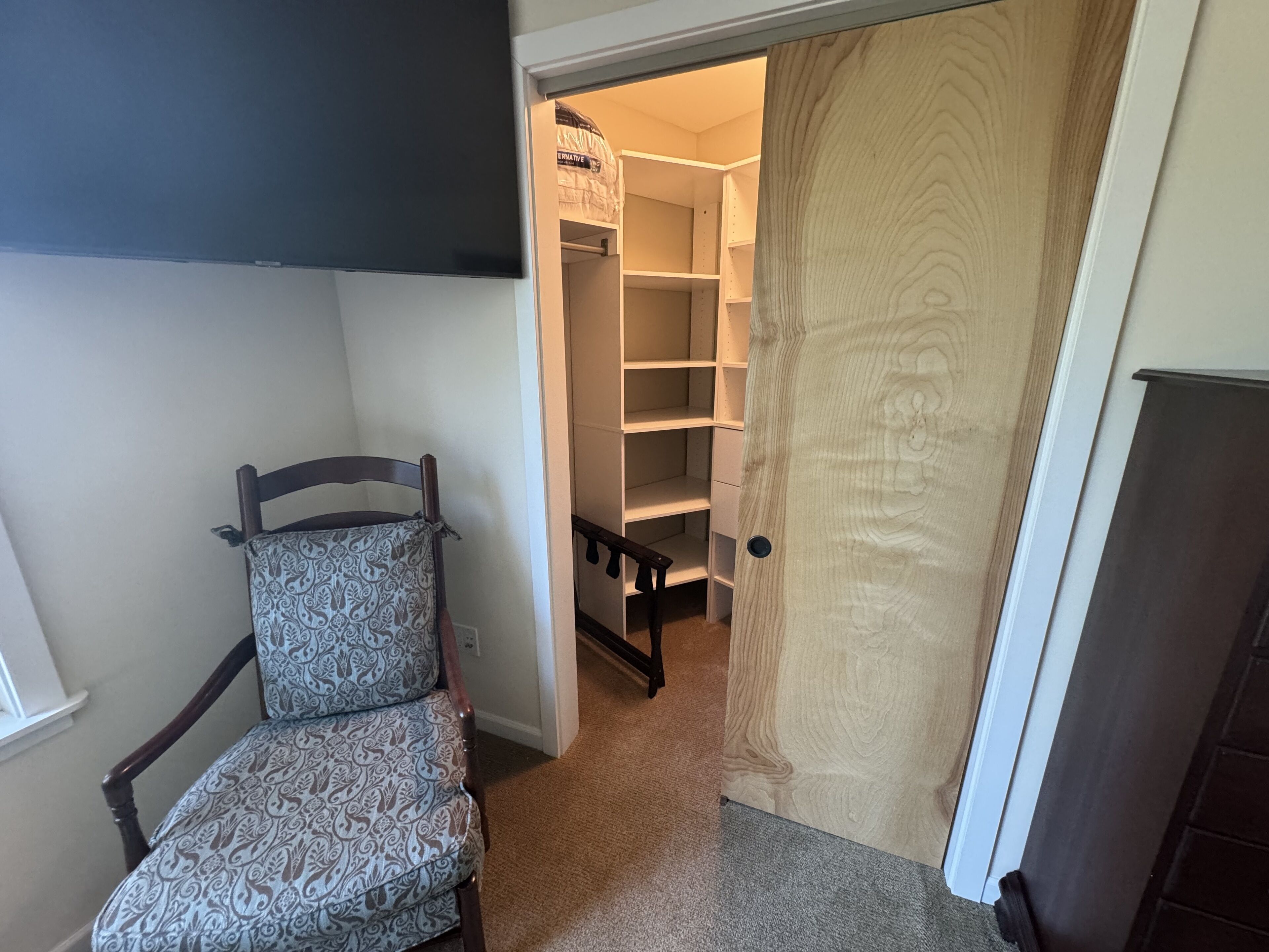 Un pasillo con una silla estampada, una puerta de madera y un armario con estantes.