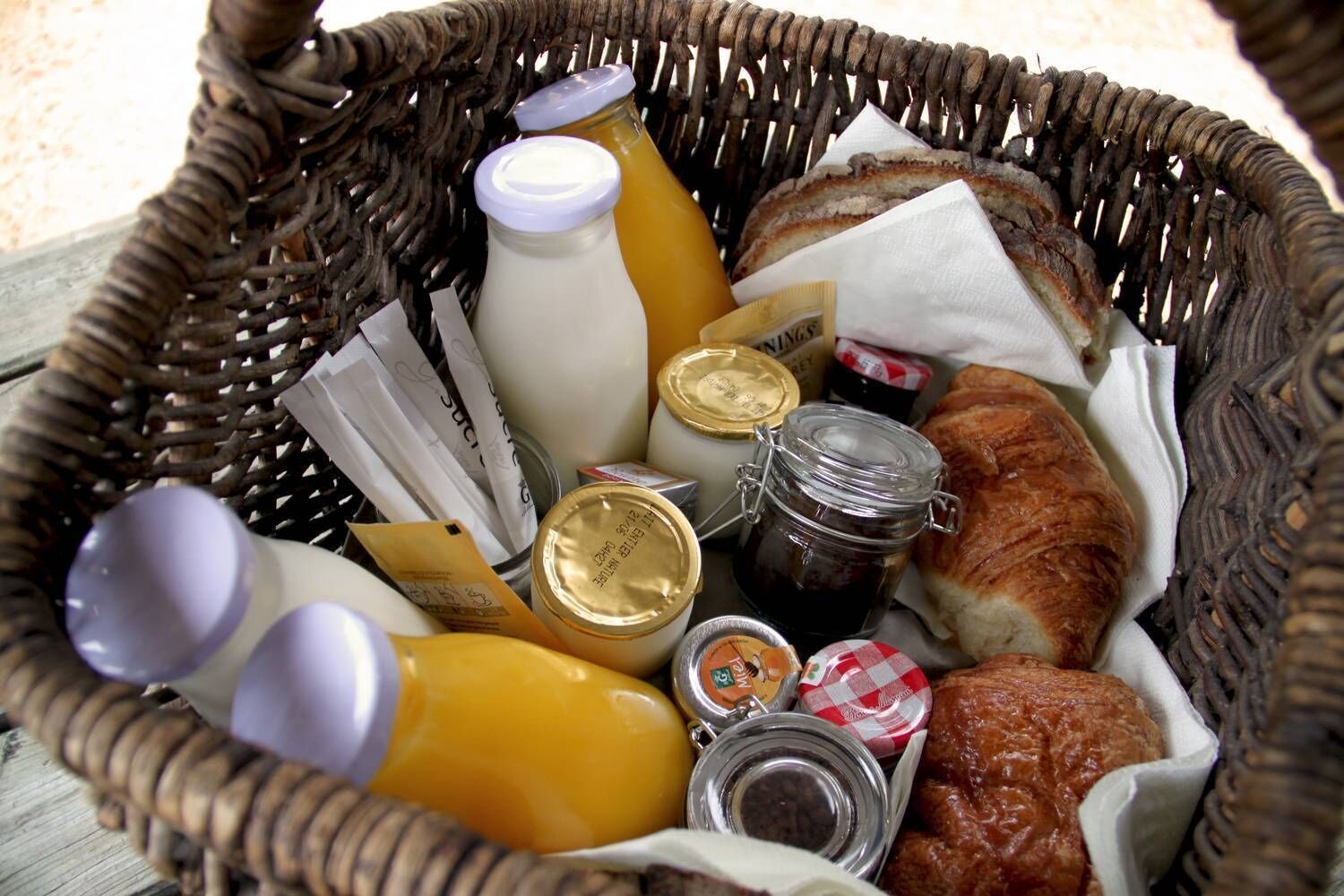 Rottinkikori, jossa on erilaisia elintarvikkeita, kuten croissant, purkkeja hilloa ja pulloja appelsiinimehua.