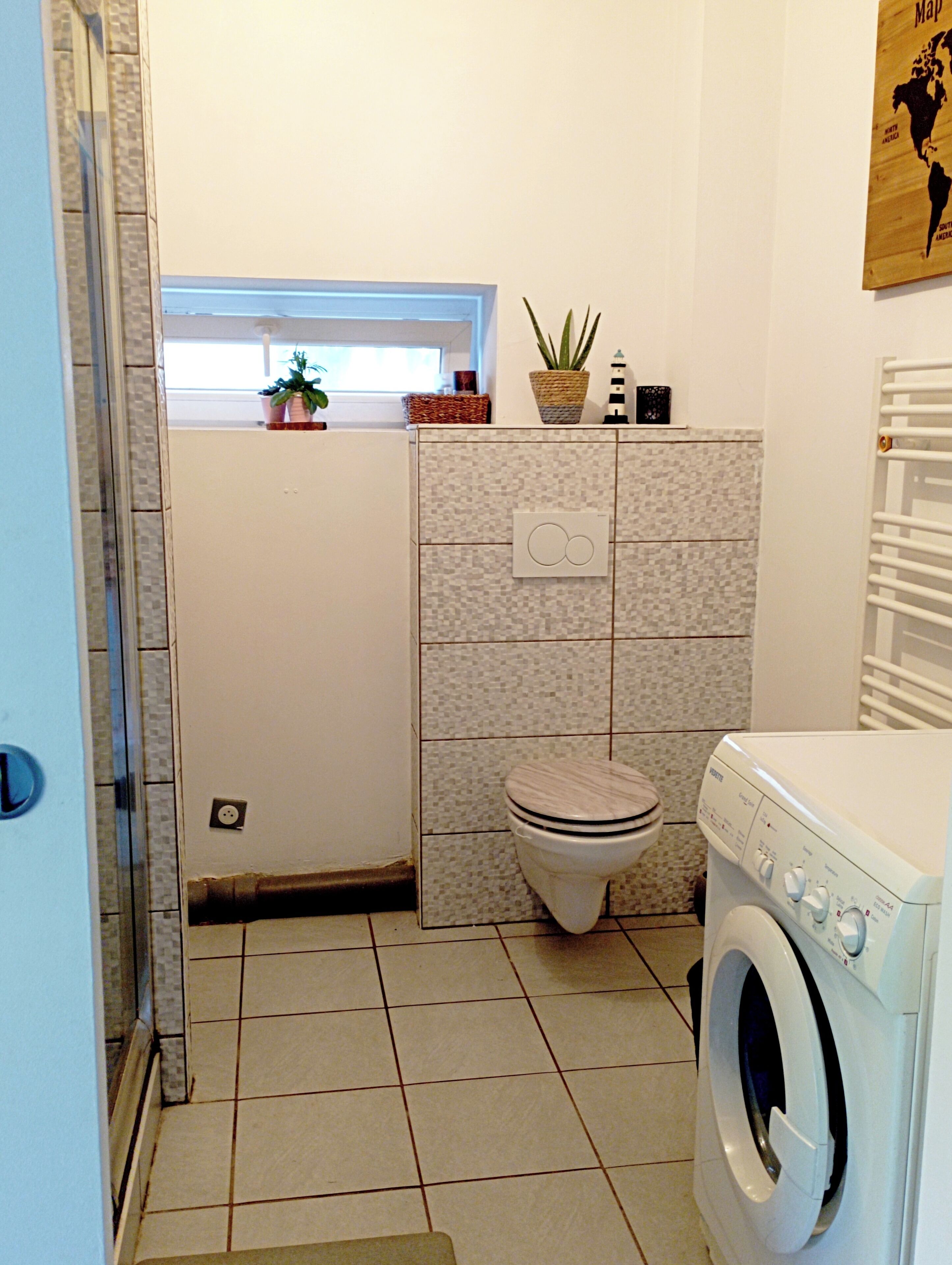 A compact bathroom with a toilet, a washing machine, and a small window.