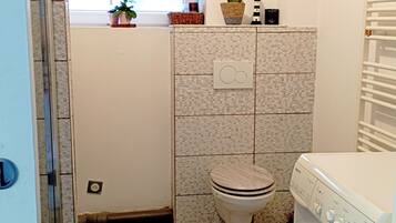 Une petite salle de bain comprenant des toilettes, un lave-linge et une petite fenêtre.