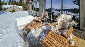 Puinen terassi, jossa on penkkejä, ja josta avautuu näkymä lumiseen maisemaan. Suuri ikkuna tarjoaa näkymän kaukaisiin vuorille.