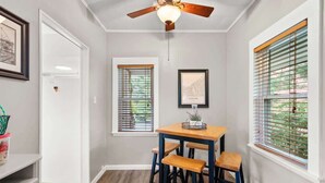 Un comedor con una mesa de madera y cuatro taburetes, un ventilador de techo y dos ventanas con persianas.