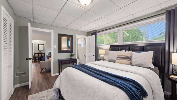 Un dormitorio con una cama grande, una mesita de noche, una ventana con cortinas y una puerta que da a otra habitación.