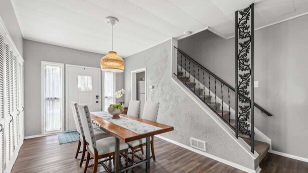 A dining area with a wooden table and chairs, a hanging light fixture, and a staircase with a decorative railing. - Double the Space for Large Groups! Entire Duplex! (Cleveland)