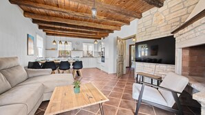 A spacious living area with a wooden ceiling, a stone fireplace, and a modern kitchen in the background. - Nice home in Cabrunici (Cabrunici)