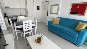 Ein kompakter Wohnbereich mit einer Küchenzeile, einem blauen Sofa, einem weißen Couchtisch und einer kleinen Essecke.