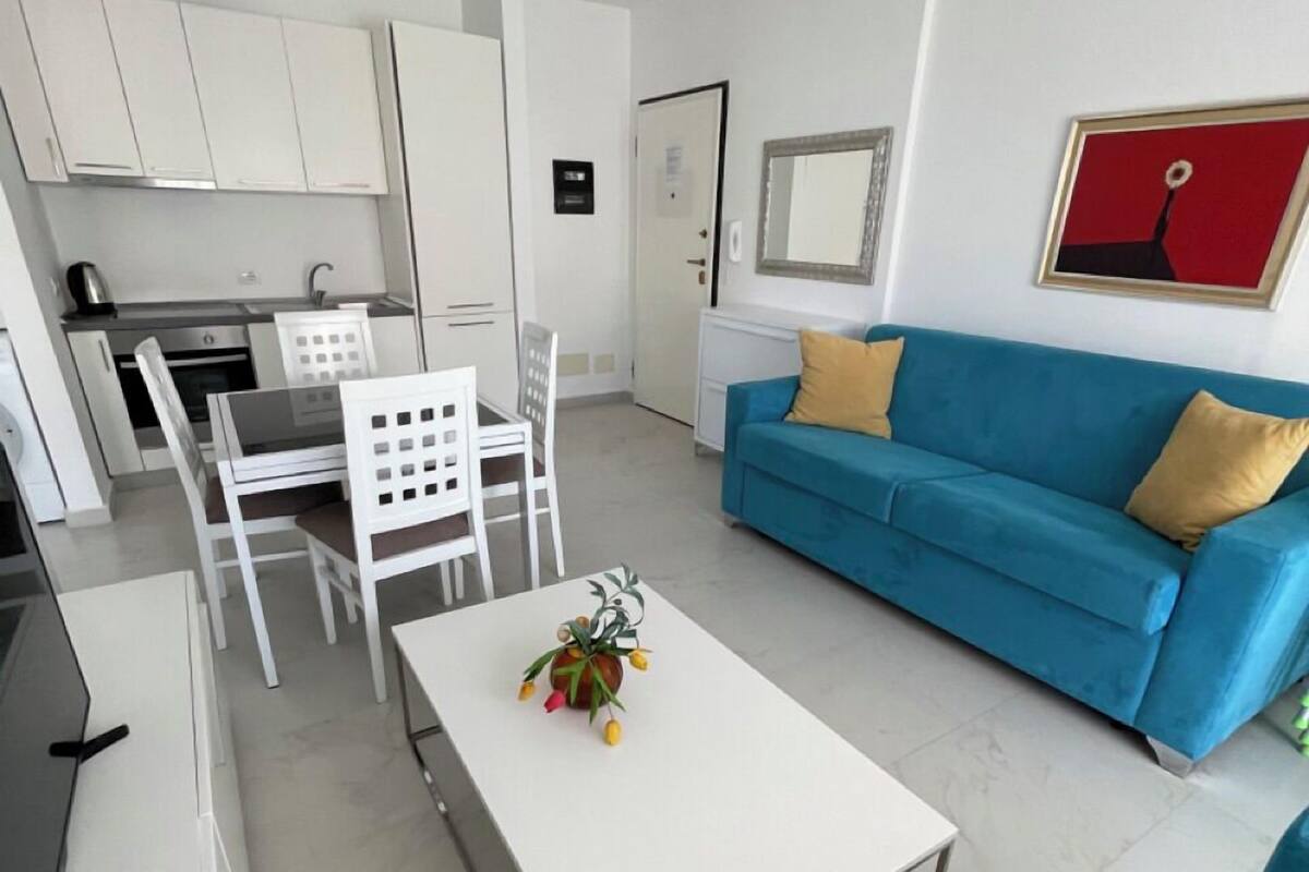 A compact living space with a kitchenette, a blue sofa, a white coffee table, and a small dining area.
