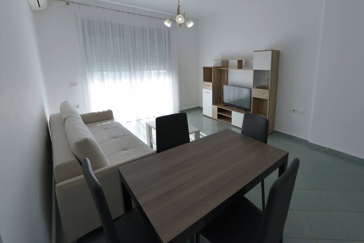 A modern living room with a sofa, a dining table, and a TV stand.