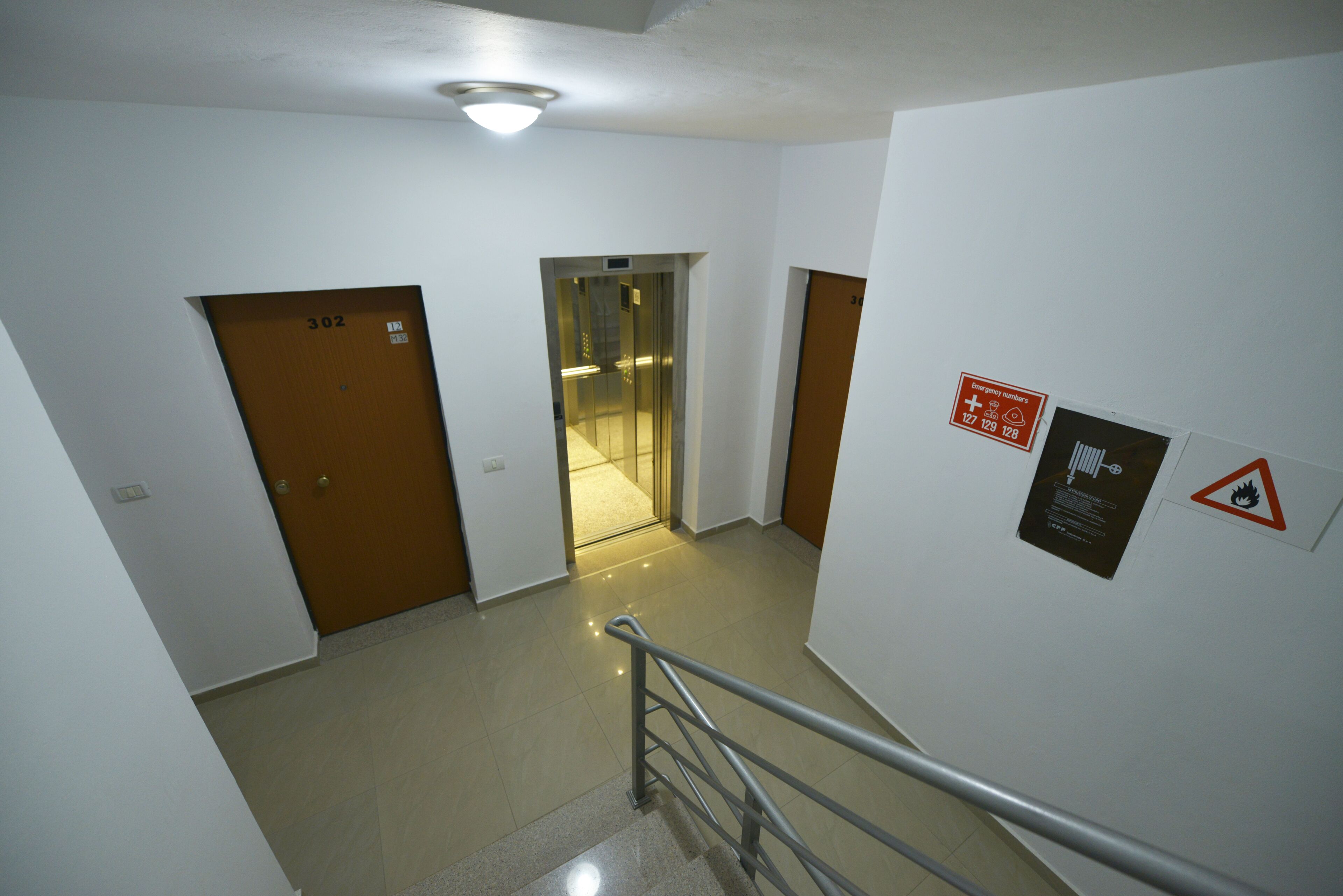 A hallway with a staircase, doors, and emergency exit signs.