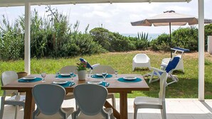 Un espace de restauration en plein air avec une table en bois prévue pour quatre personnes, entourée de chaises blanches.
