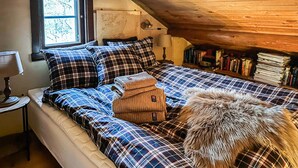 A cozy attic bedroom with a sloped ceiling, a bed with plaid bedding, a lamp, and a bookshelf filled with books. - Cozy home in Fjärås with house sea view (Fjärås)