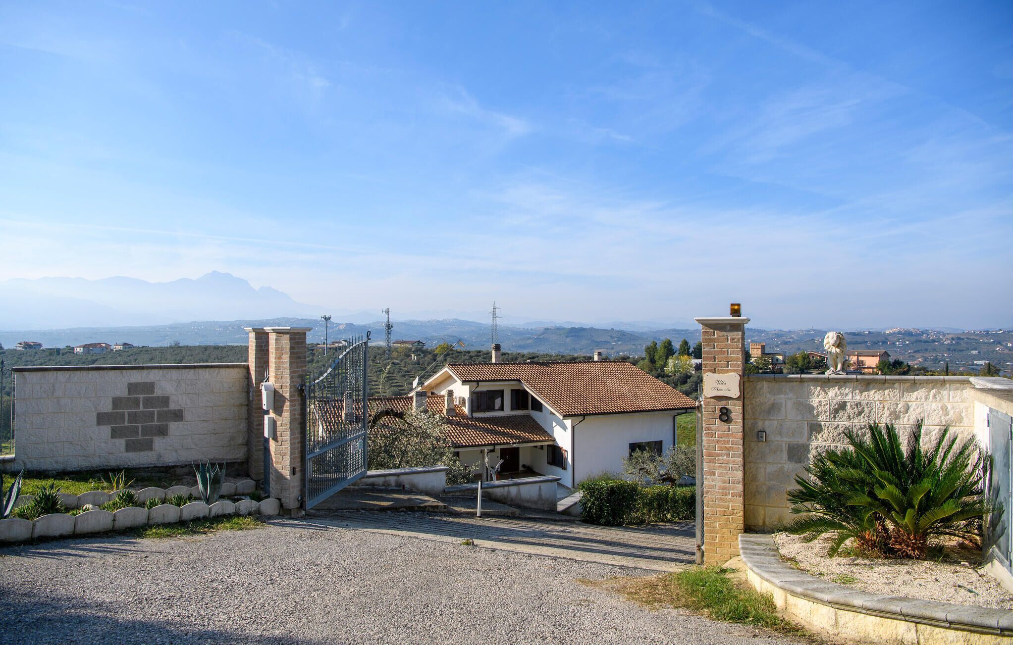 A residential property with a gated entrance, a small house with a tiled roof, and a view of distant mountains and a cityscape.