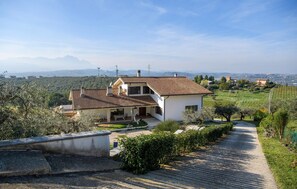 A two-story house with a tiled roof, surrounded by greenery and a clear view of distant mountains.