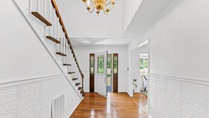 A hallway with a wooden staircase, white walls, and a chandelier.