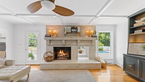 A living room with a fireplace, a ceiling fan, and a view of a swimming pool.
