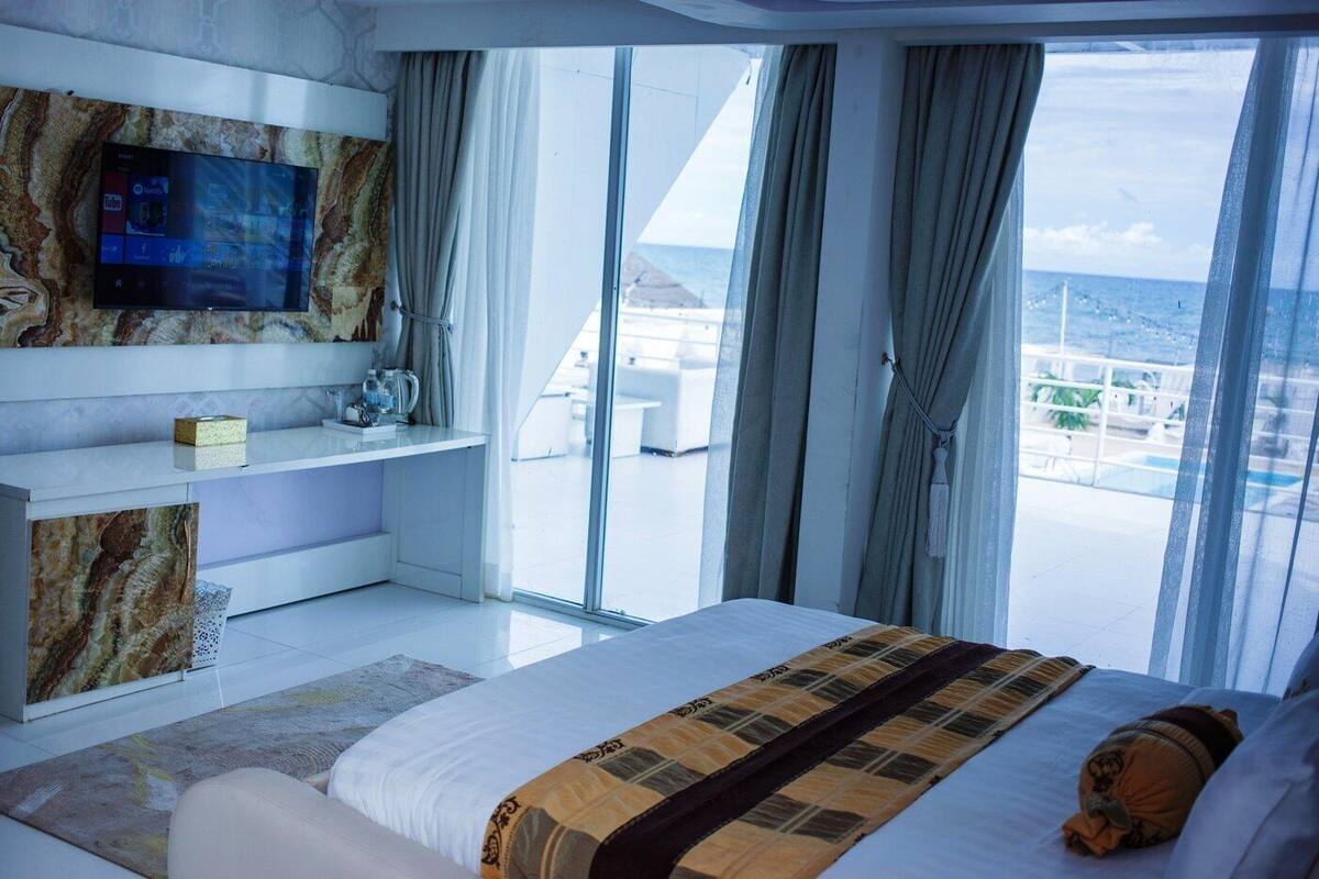 Ein modernes Hotelzimmer mit einem großen Bett, einem Wand-Fernseher und einem Balkon mit Blick auf den Pool.