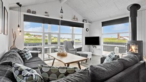 A spacious living room with a large sofa, a coffee table, and a fireplace. There are multiple windows providing a view of the outdoors. - Beautiful home in Hejls with WiFi (Hejls)
