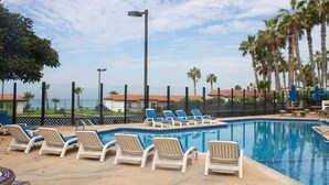 Zona de piscina con sillas de descanso y vista al océano.