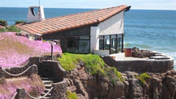Un edificio costero con techo de tejas, amplias ventanas y vista al mar.