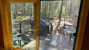 A wooden deck with outdoor seating and a covered grill area, overlooking a forested area. - New Spacious Acadia Timberframe, Close to Swimming, Central to Hiking and Dining (Mount Desert)