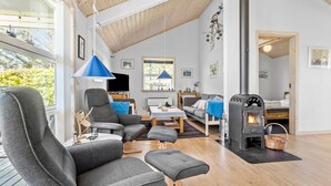 A modern living room with a high ceiling, a fireplace, and a large window overlooking greenery. - 3 bedroom amazing home in Vestervig (Vestervig)