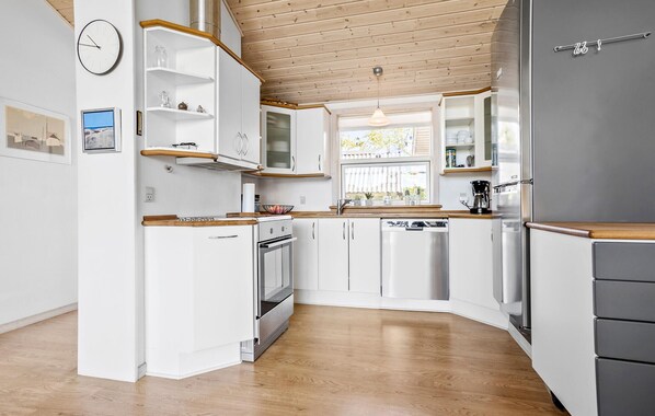 Une cuisine moderne avec des meubles blancs, un réfrigérateur en acier inoxydable et des plans de travail en bois.