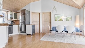 A modern kitchen with a large refrigerator, a coffee maker, and a dishwasher. There is a dining area with a table and chairs, and a rug on the floor. - 3 bedroom amazing home in Vestervig (Vestervig)