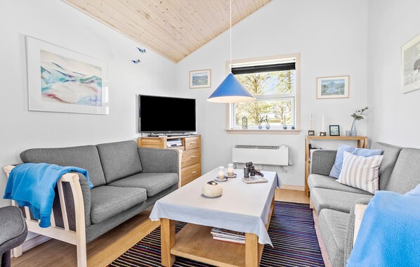 A modern living room with a grey sofa, a small table, a TV, and a window with a view of trees. - 3 bedroom amazing home in Vestervig (Vestervig)
