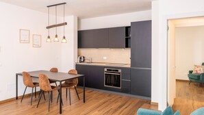 Une cuisine moderne avec des meubles de couleur sombre, une table à manger en bois avec des chaises et des luminaires suspendus.